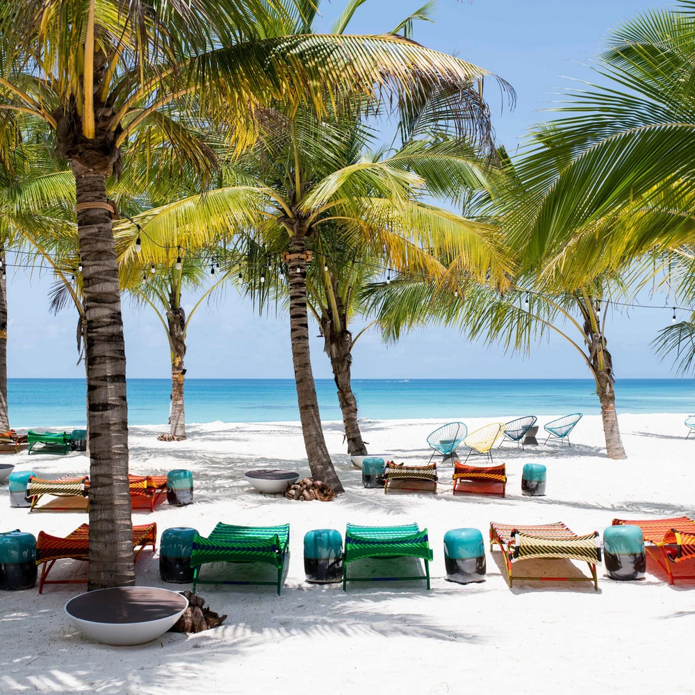 Colourful green and orange loungers under palms on white sand beach