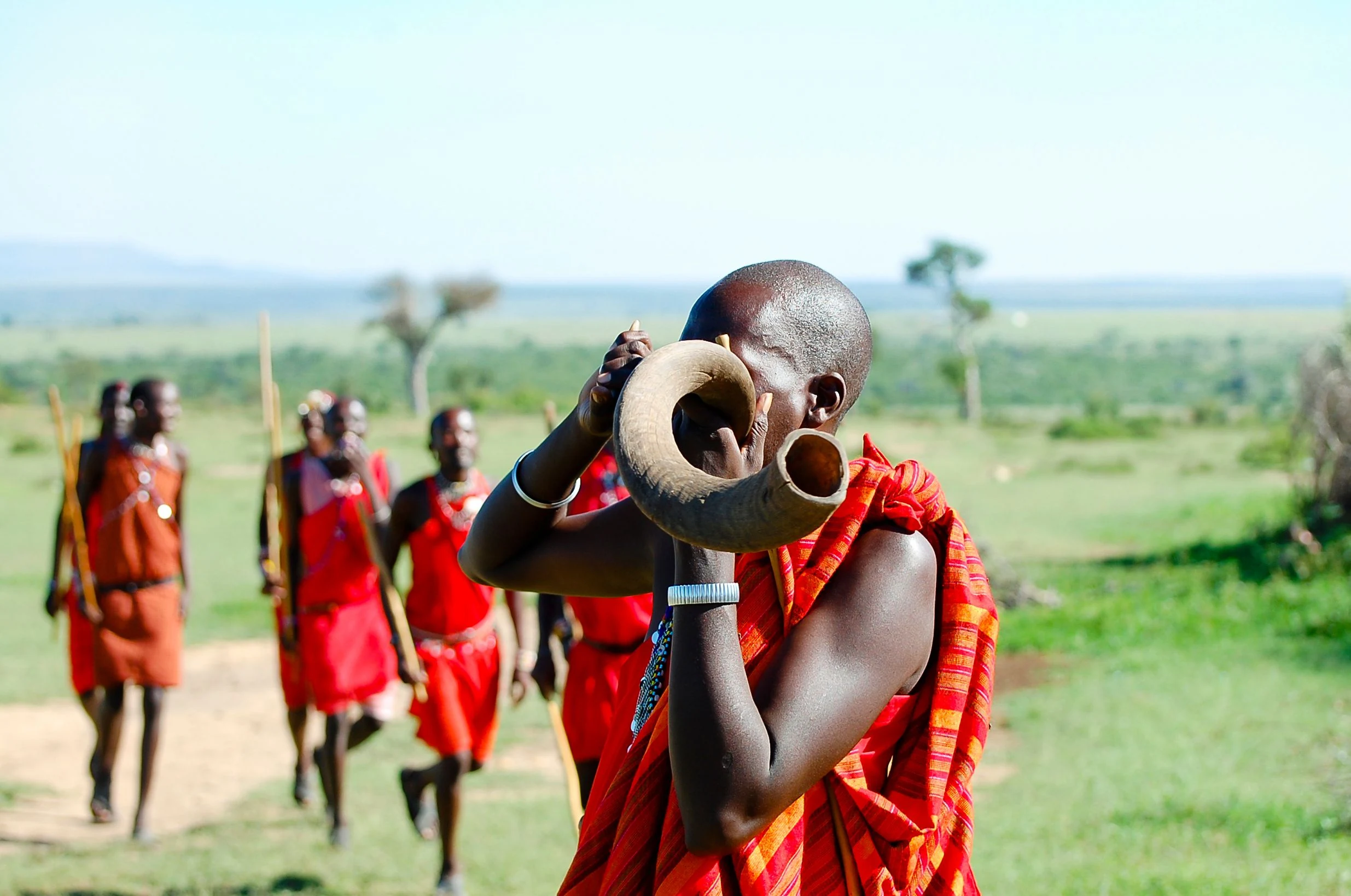 Maasai guide sounding a kudu horn with others walking behind