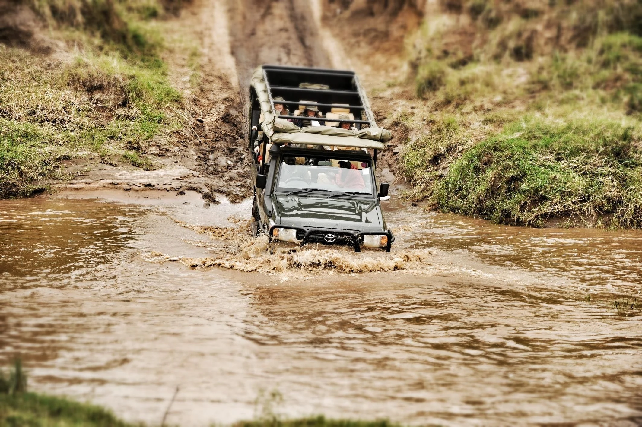 A safari vehicle driving through a muddy river crossing in Mara North