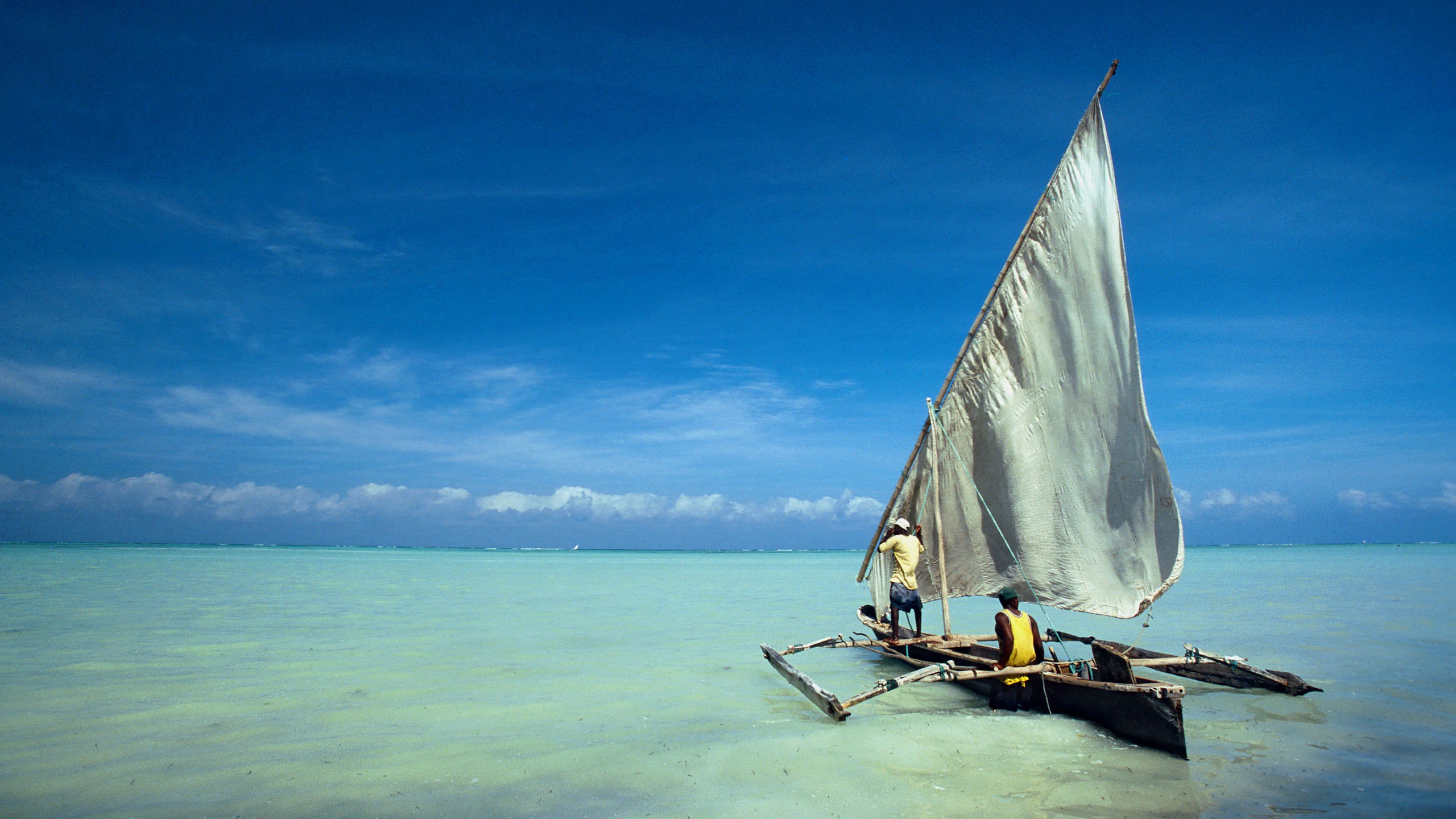 Outrigger dhow with two men on pale turquoise lagoon