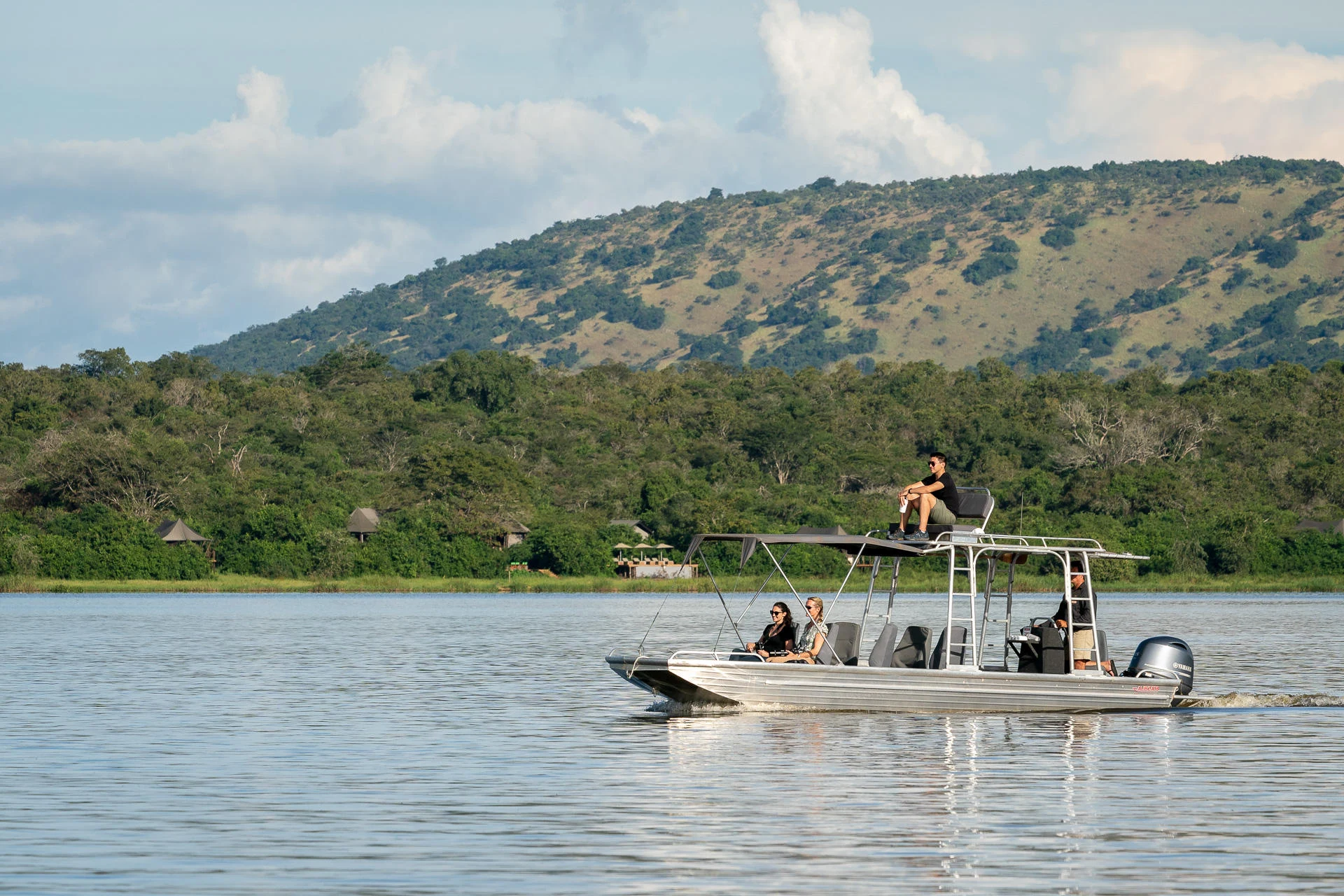 A small motorboat with passengers cruising a lake below wooded hills in Akagera