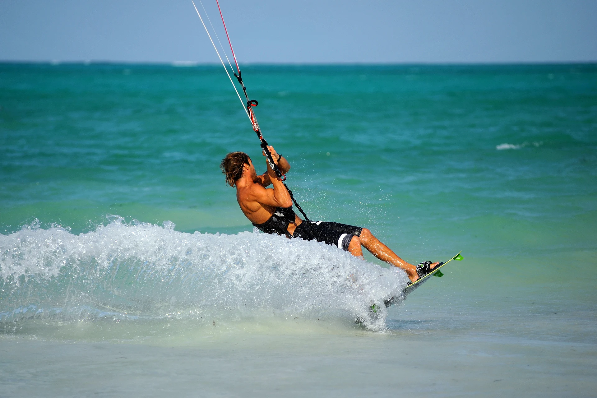 A kitesurfer carving through spray across turquoise water off Zanzibar