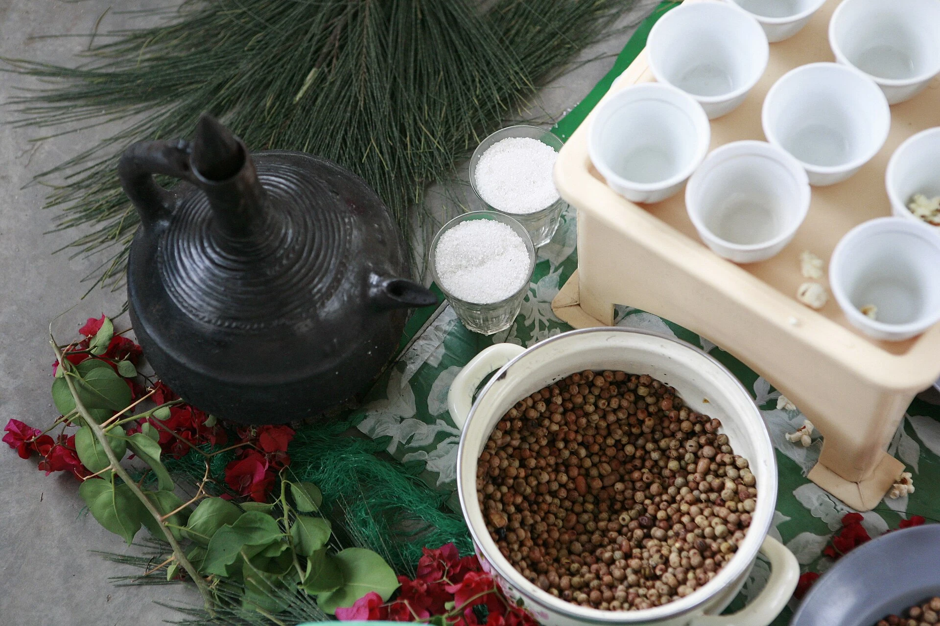 A clay coffee pot, roasted beans and small cups laid out for a coffee ceremony.