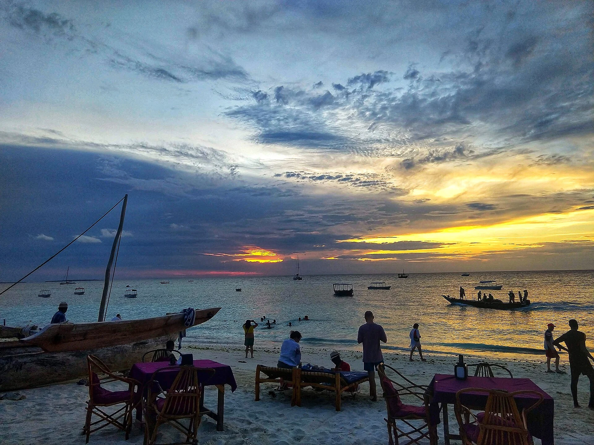 A dhow and beach tables at Nungwi under a cloudy sunset sky
