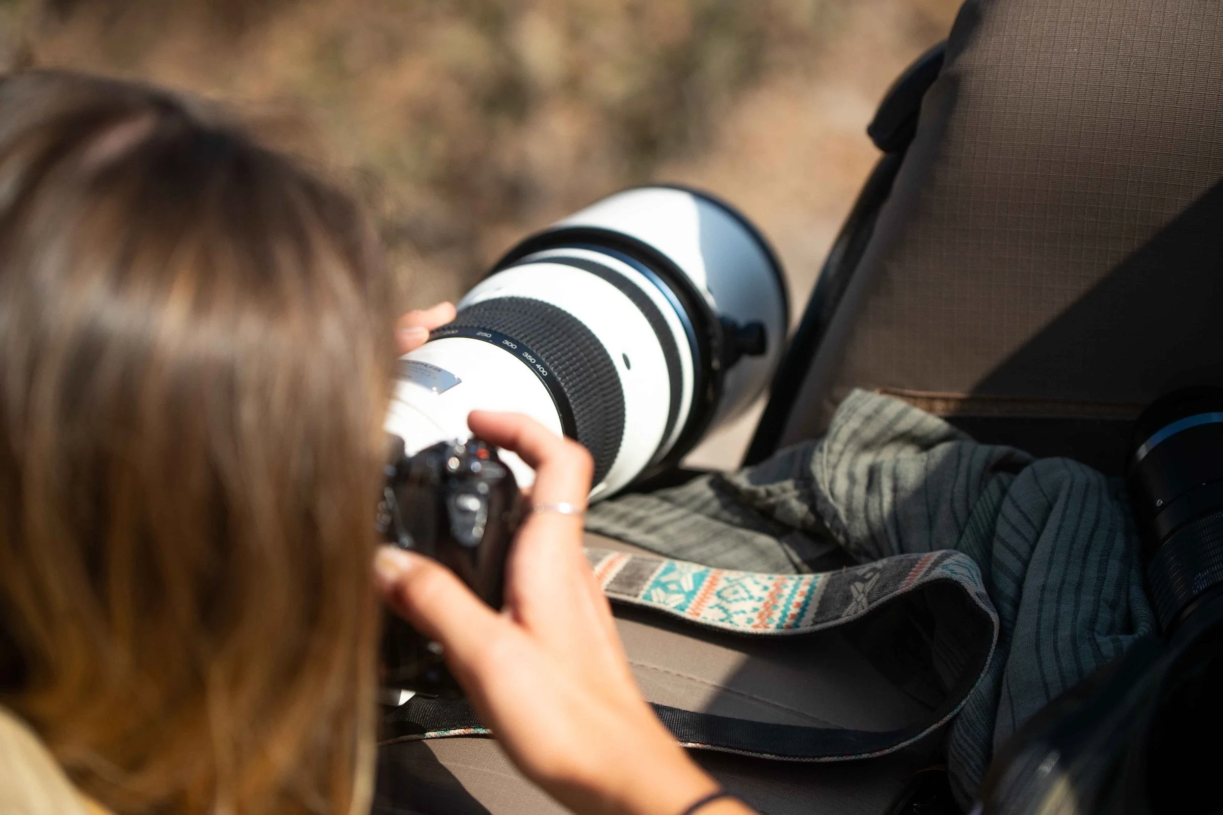 A guest steadies a camera with a long white lens on a folded cloth in an open safari vehicle