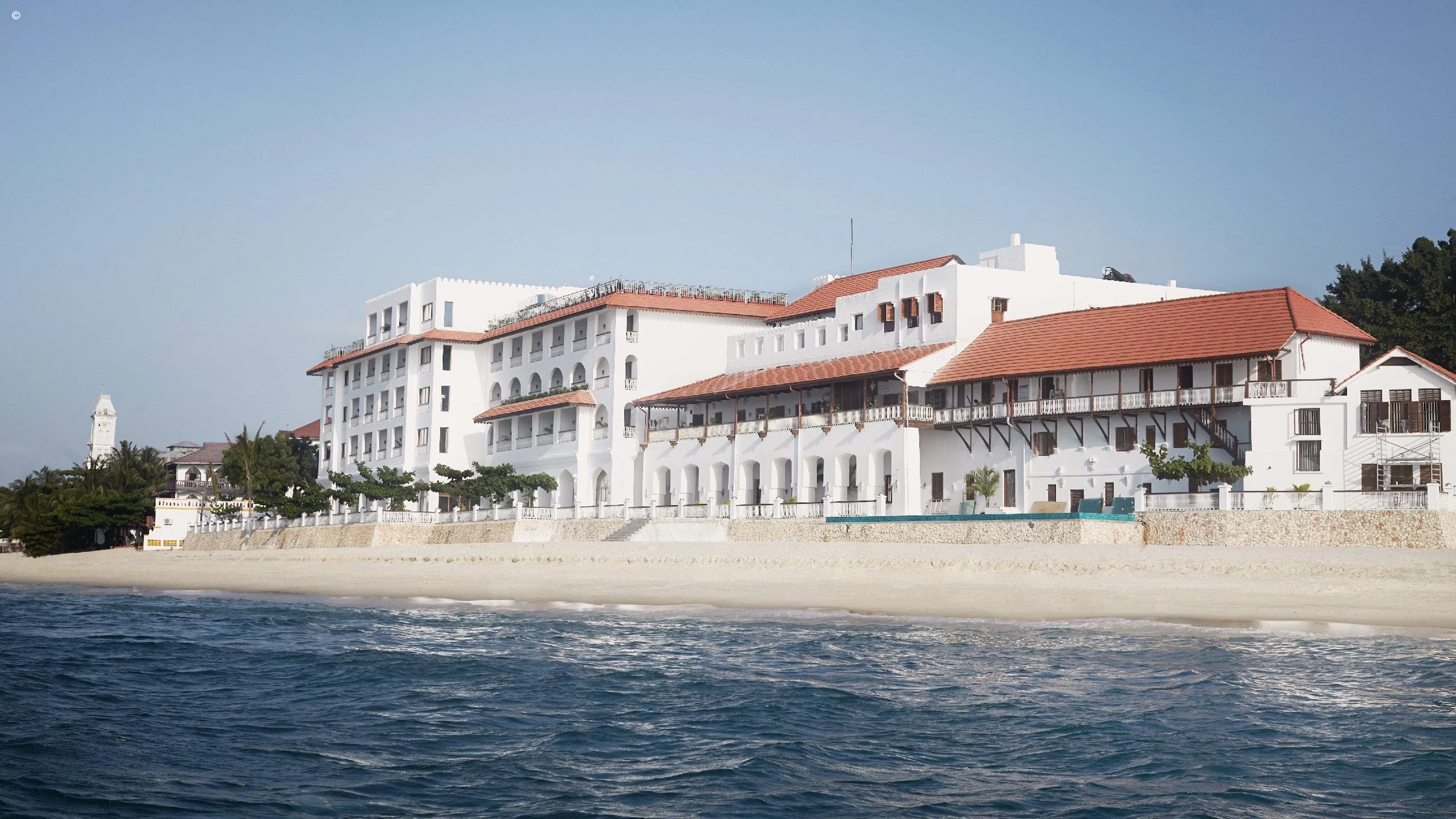 White hotel with red roofs on the Stone Town seafront from the water at Park Hyatt Zanzibar