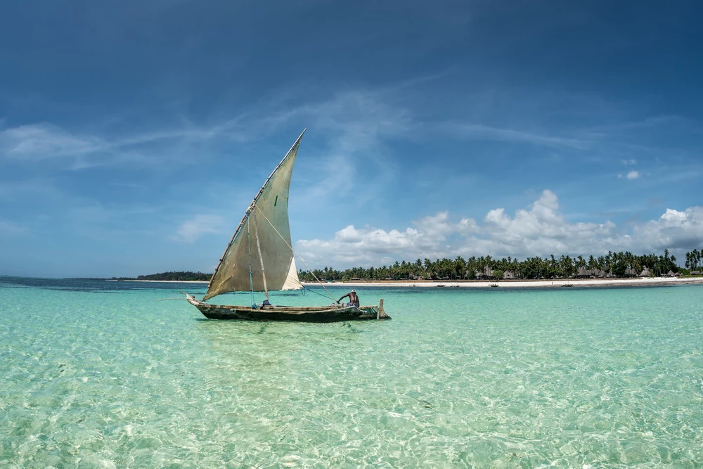 A dhow sailing across clear turquoise shallows off Kenya's coast