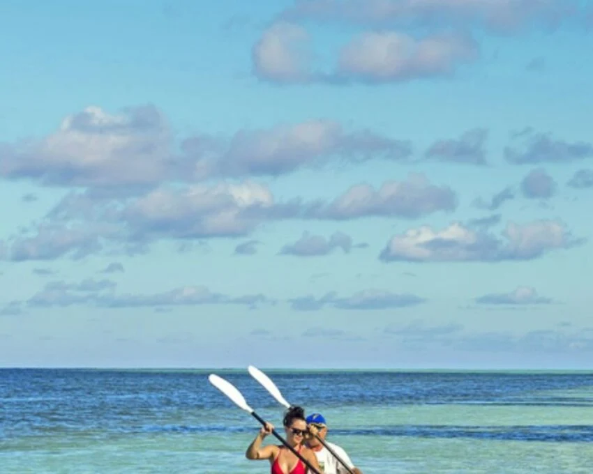 Two kayakers paddling in shallow water beneath a wide hazy sky