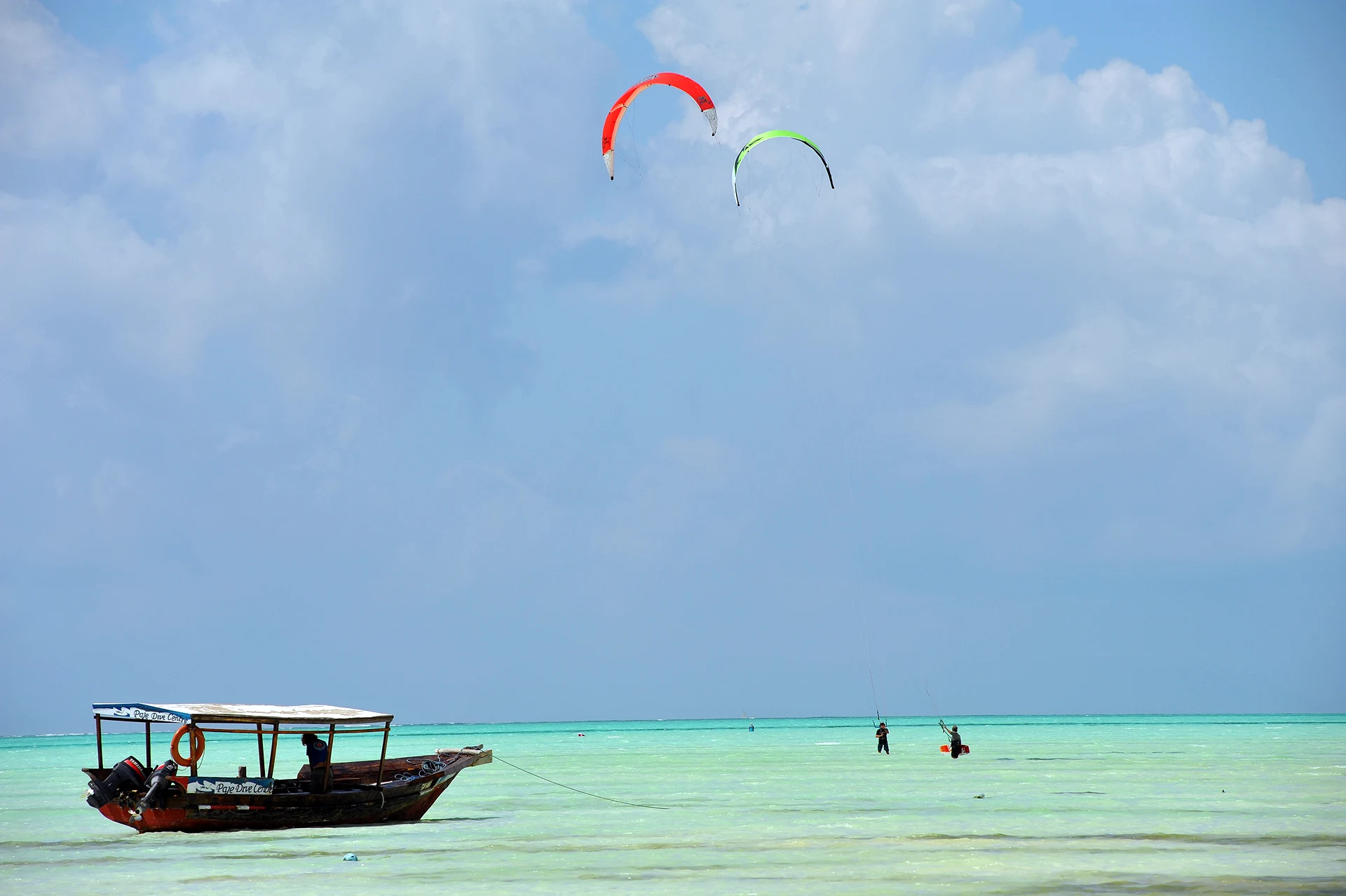 Kites in the sky above a moored boat and people in shallow Zanzibar water
