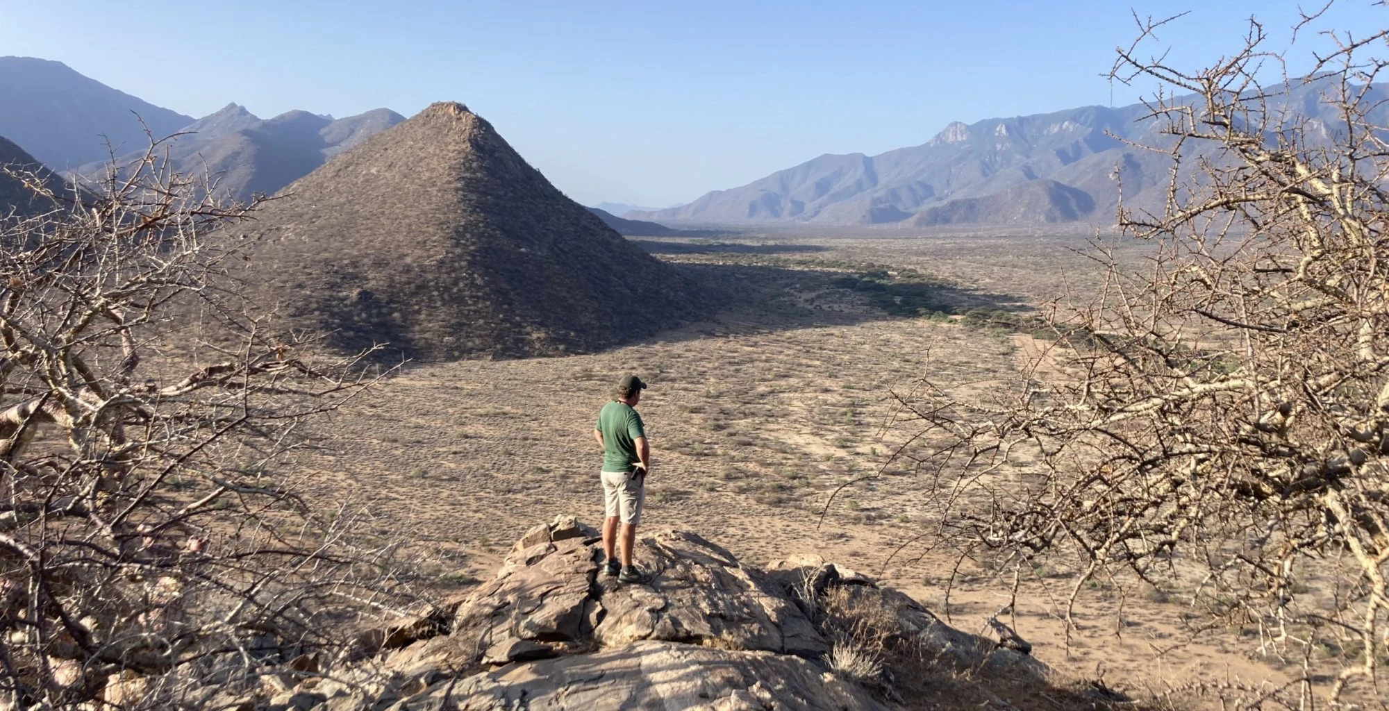 A hiker stands on a rocky outcrop overlooking a wide mountain valley