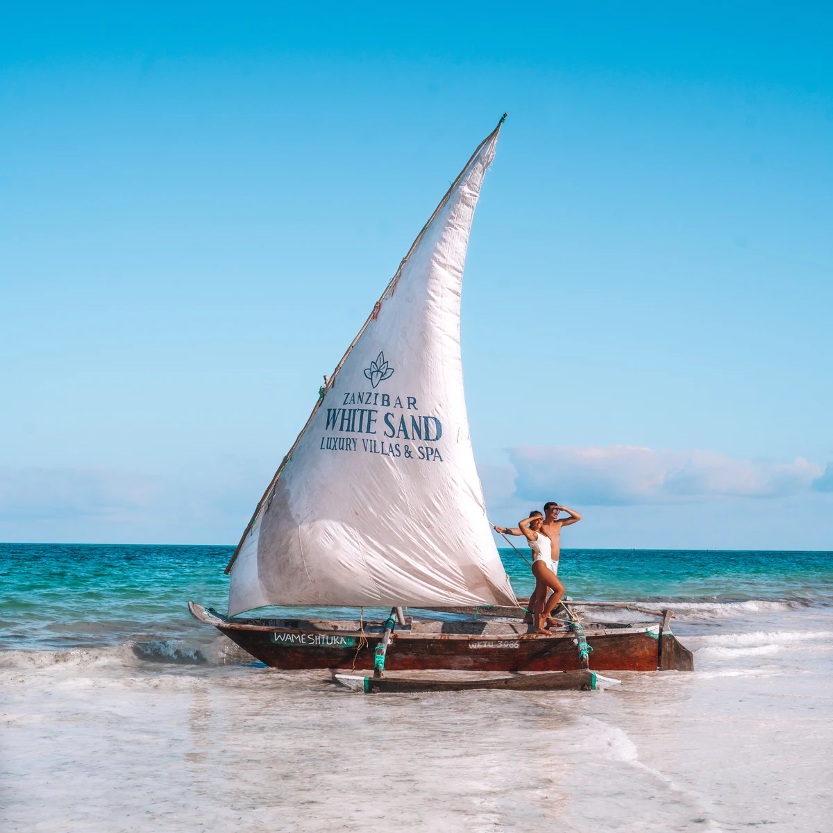 Dhow with printed sail on shallow water, woman standing aboard