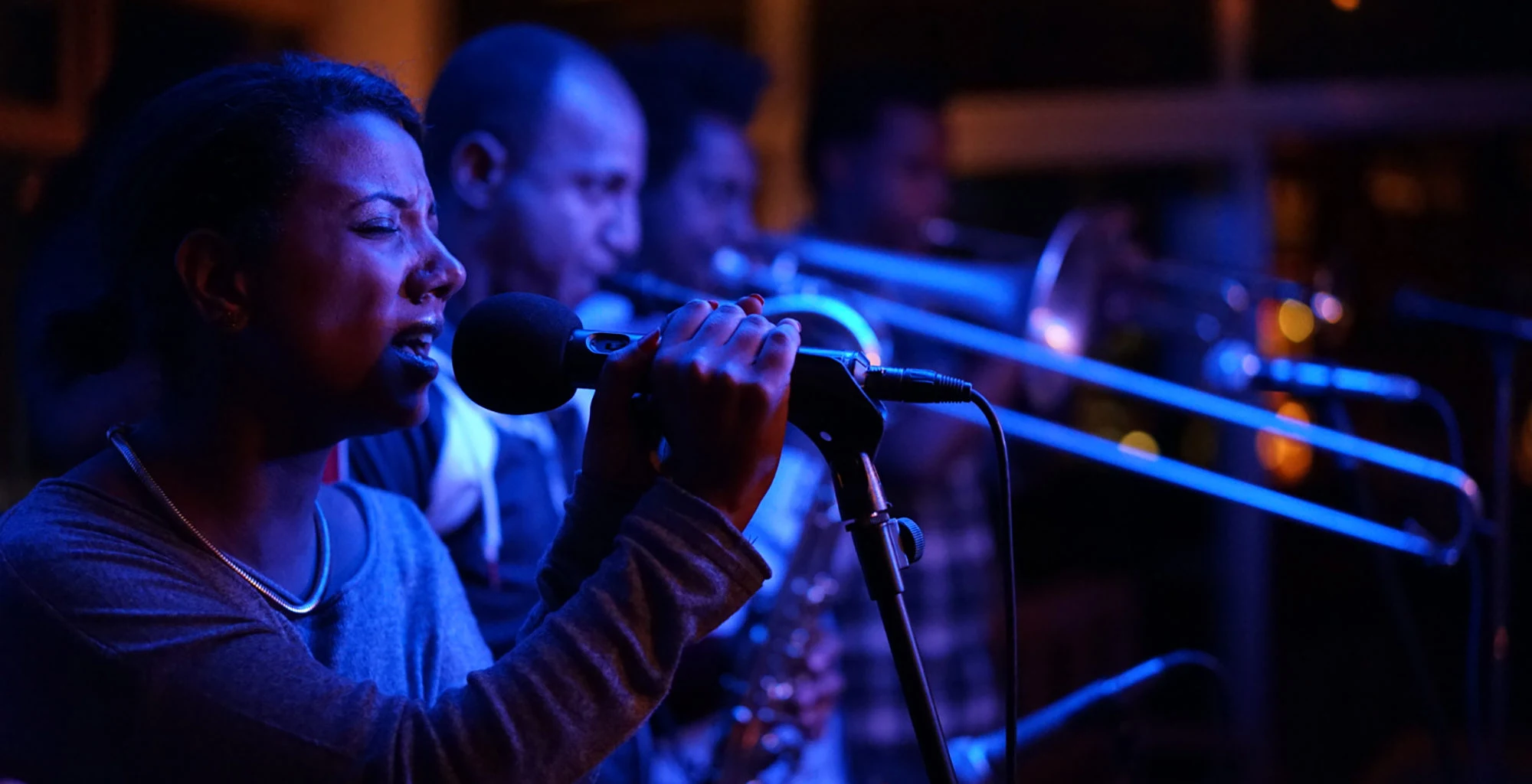 A singer and horn players perform on stage under blue lights.