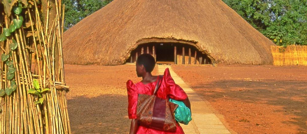 Woman in a red gomesi approaching the thatched royal tomb at Kasubi, Kampala