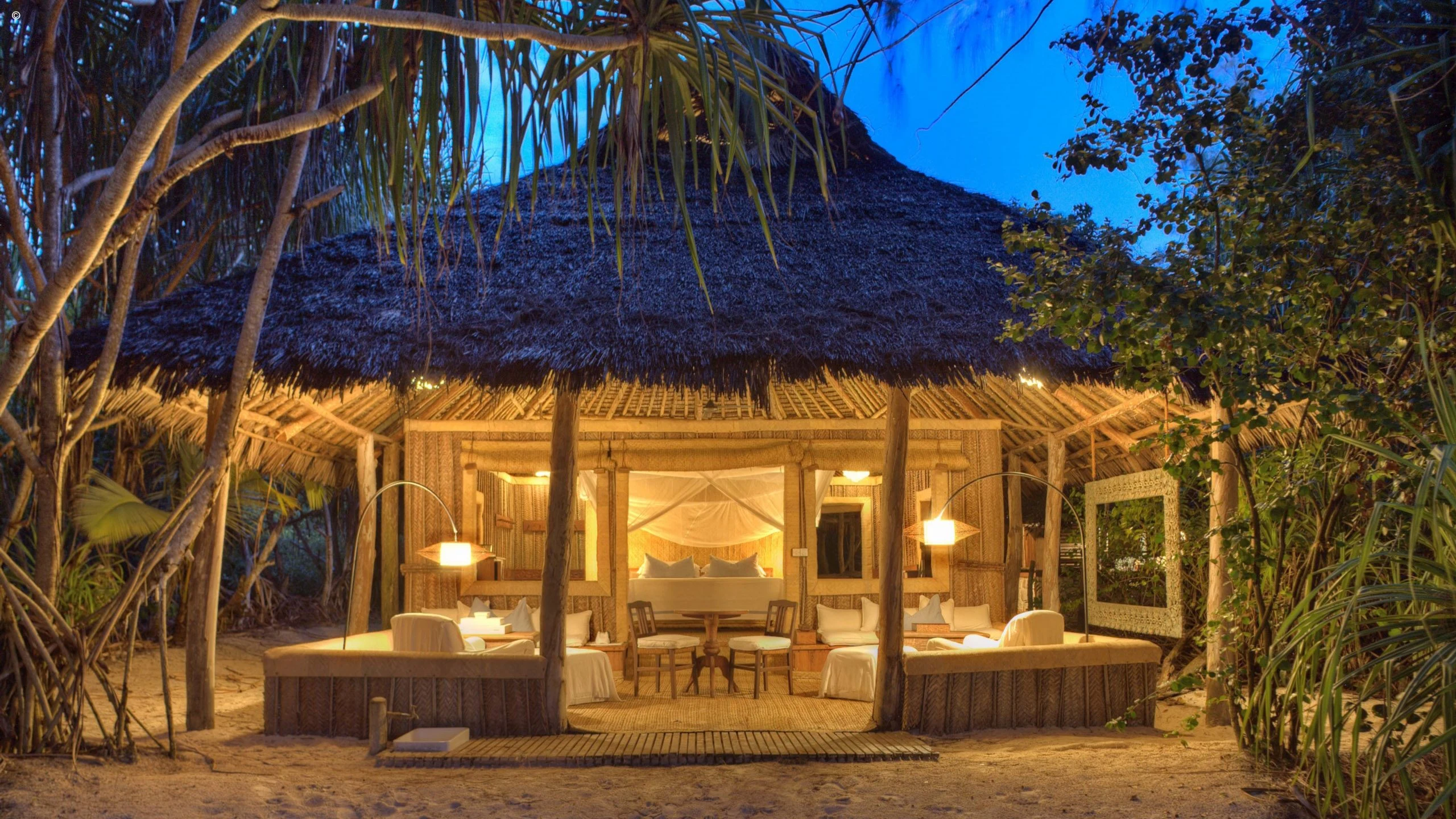 Thatched beach villa glowing at dusk among trees at Mnemba Island Lodge