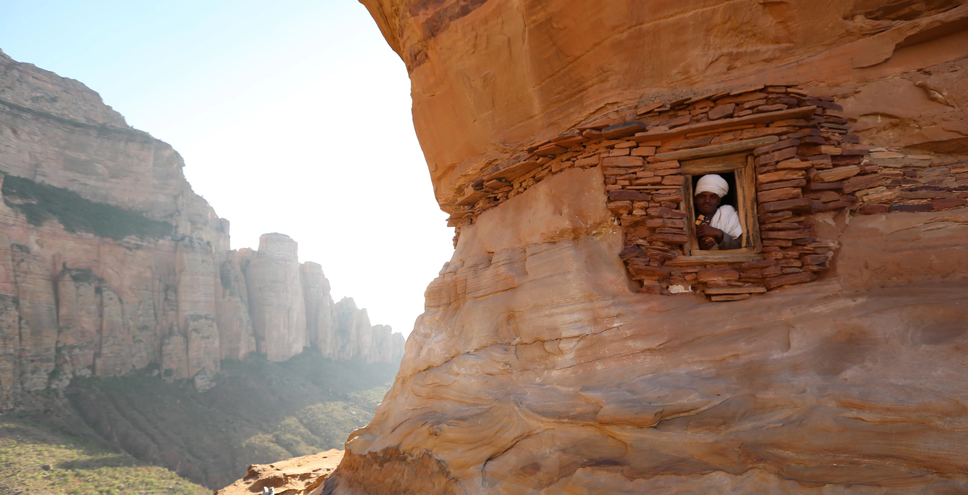 A figure sits in the cliff-face doorway of the Abuna Yemata Guh church.