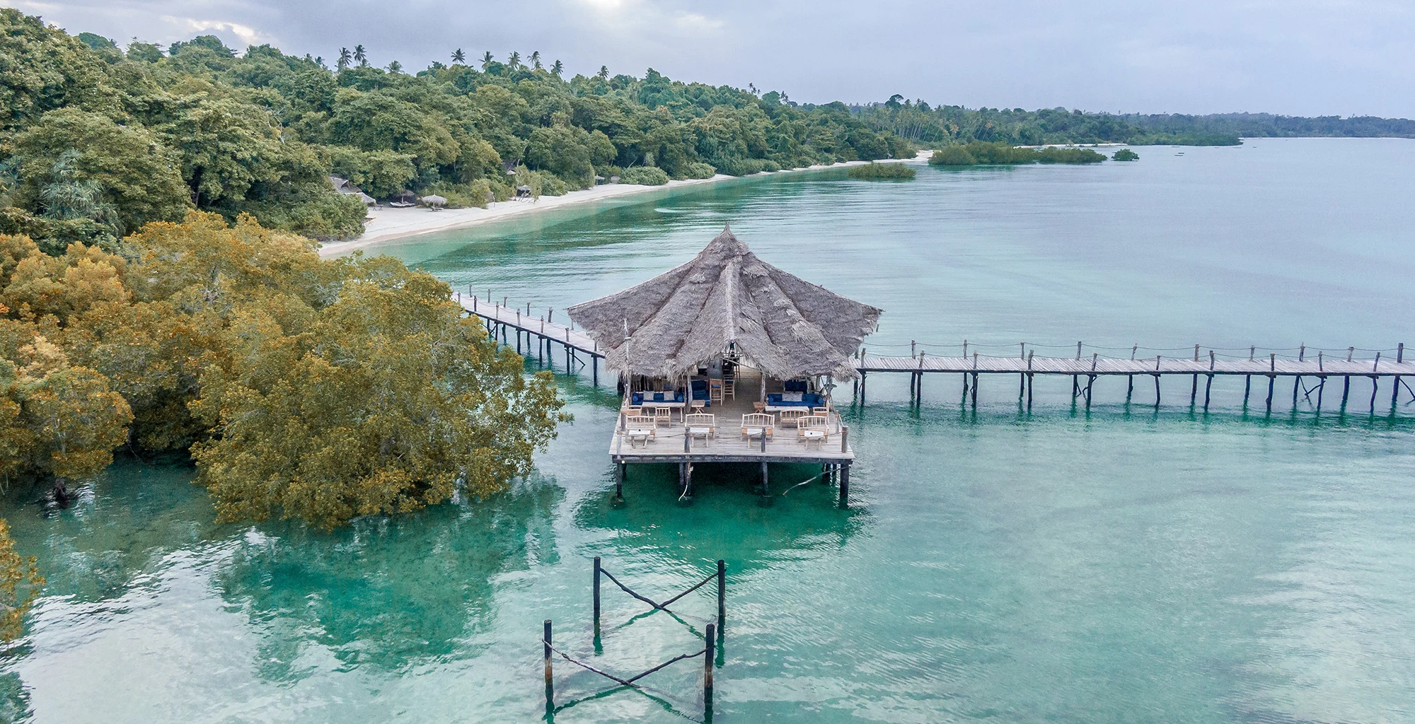 A wooden jetty running past mangroves to a thatched pavilion over the lagoon