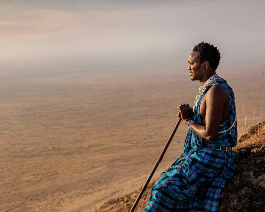 Maasai man in blue sitting on a ridge above a hazy valley