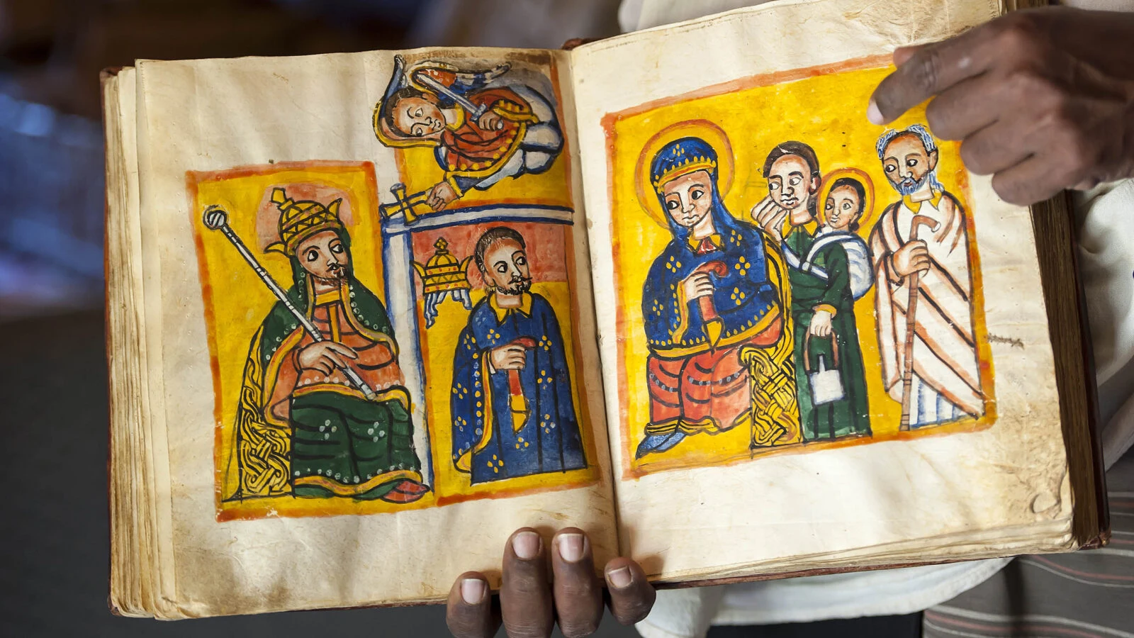Hands holding an open illuminated manuscript with painted figures