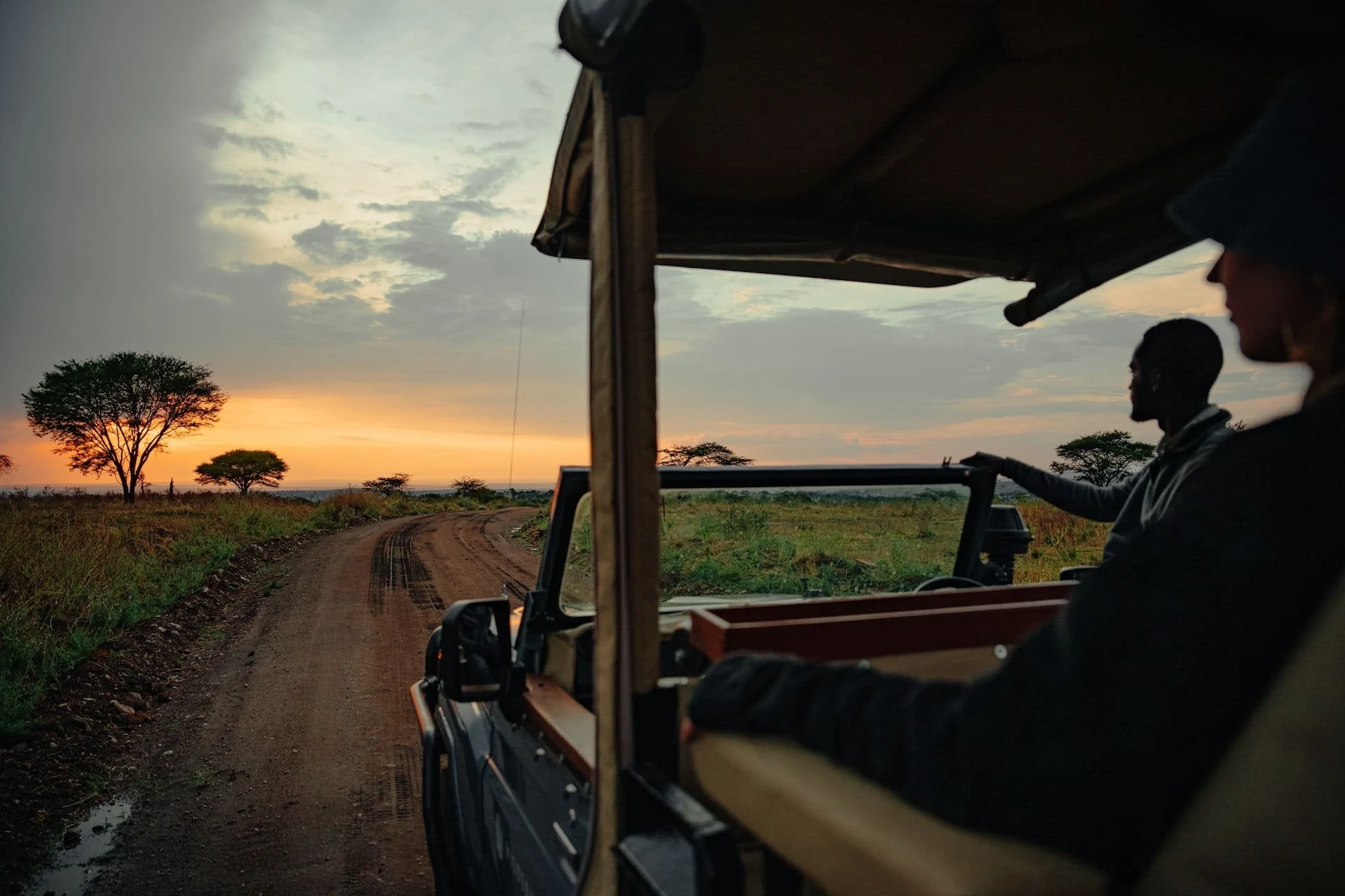 Silhouetted guide and guest in open vehicle looking at sunset