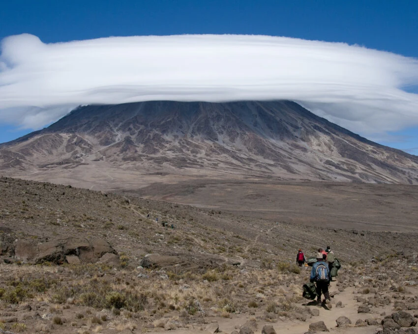 Porters walking a trail below Kilimanjaro under a lenticular cloud