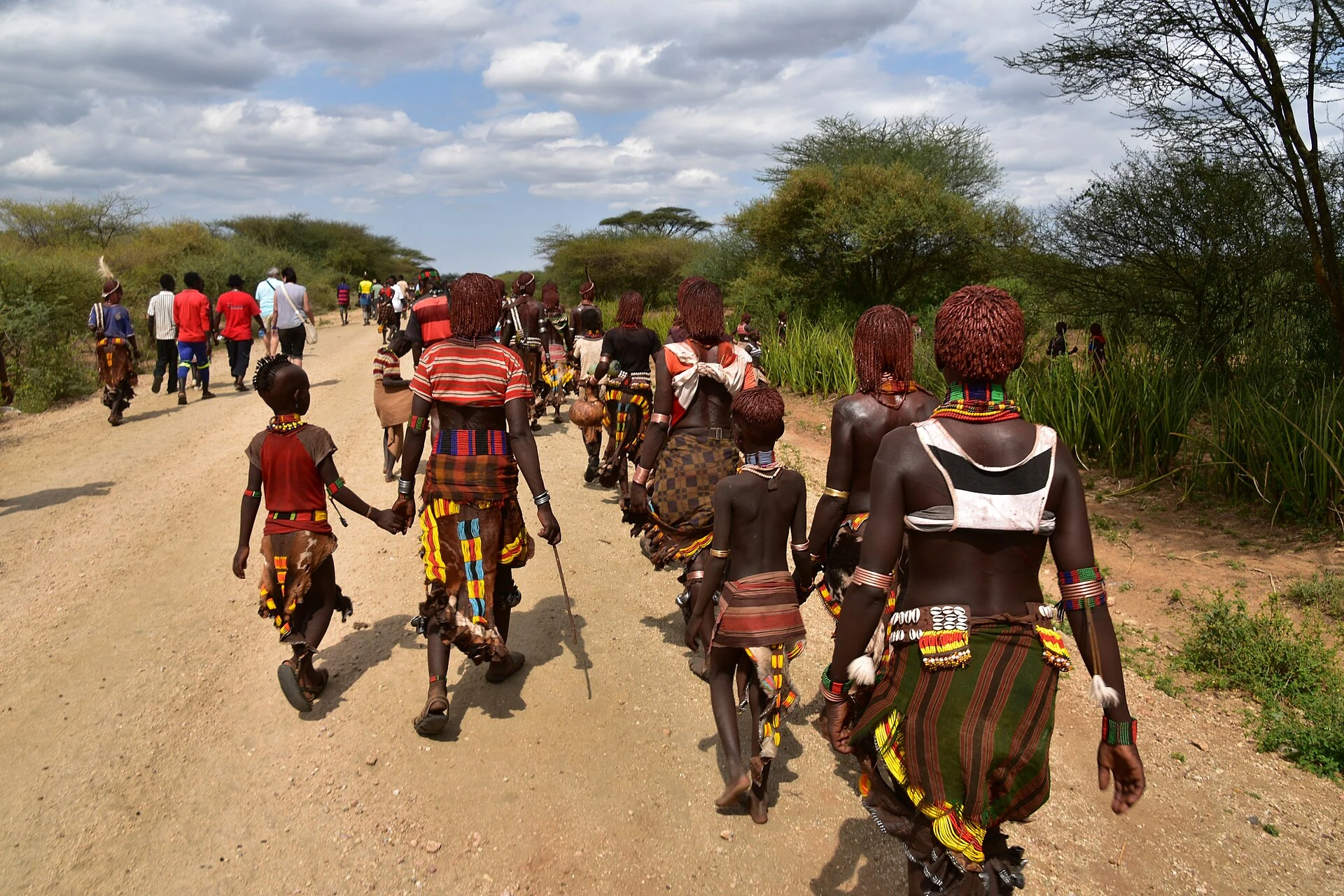 Hamer women and children walk along a dirt road to a bull-jumping ceremony.
