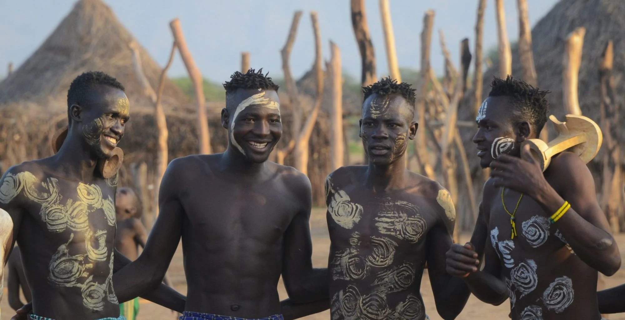 Four Karo men with white body paint laugh together in their village.