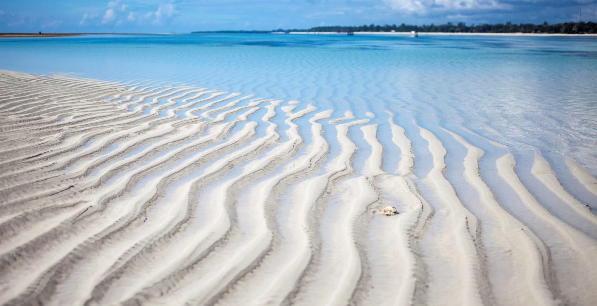Rippled white sand under clear shallow water at low tide on Galu Beach
