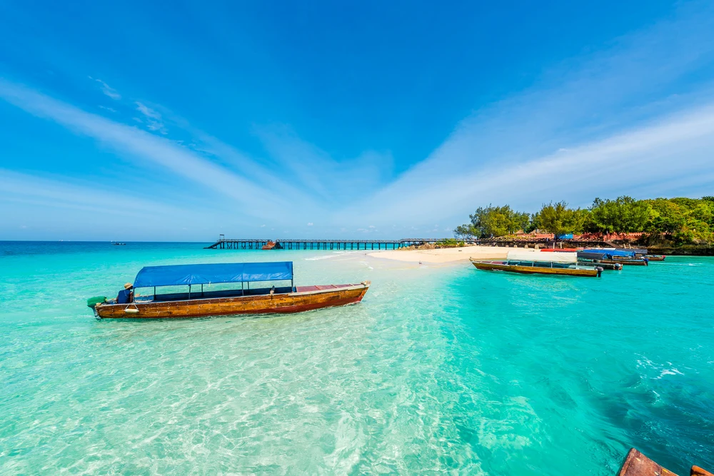 A canopied wooden boat moored in clear turquoise shallows off a beach