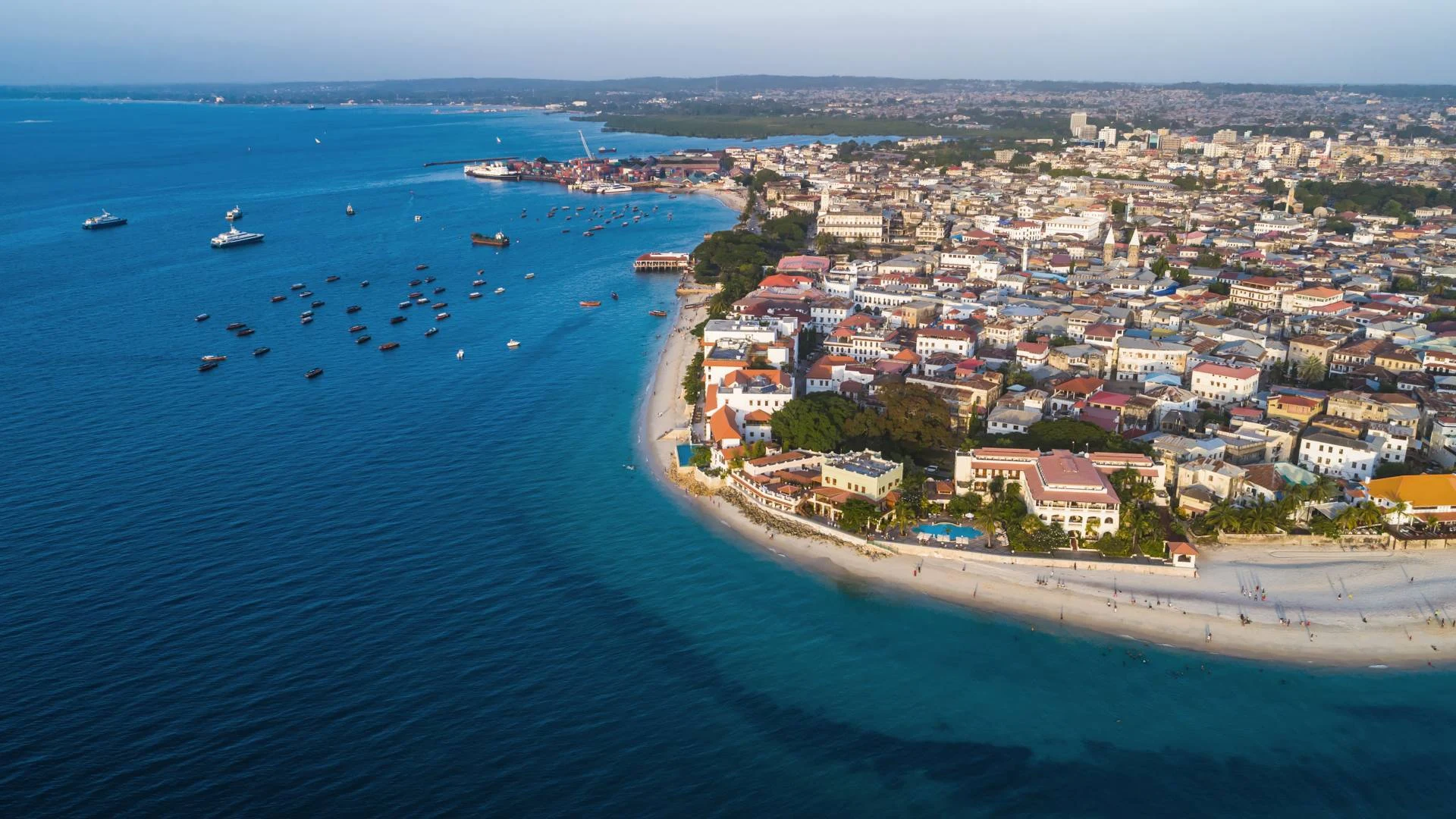 Aerial view of an old waterfront town on a curving shore with boats offshore