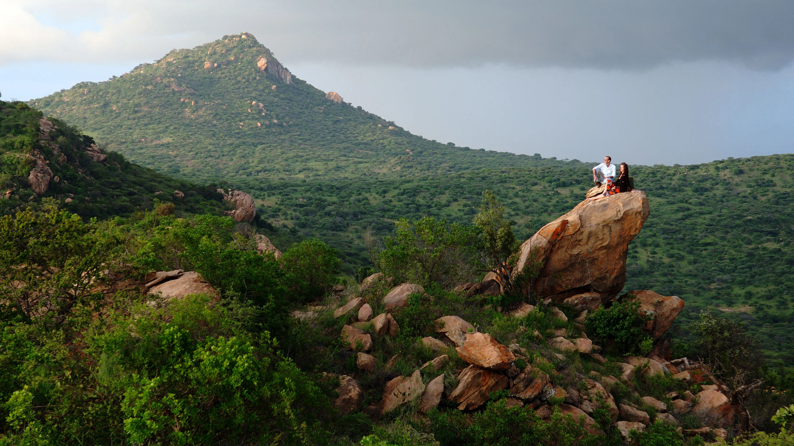 Two small figures on a boulder above wooded hills