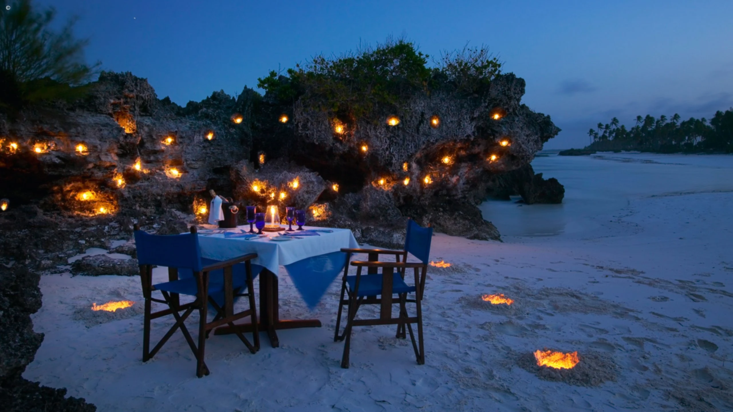 Candlelit dinner table on a beach among rocks at dusk