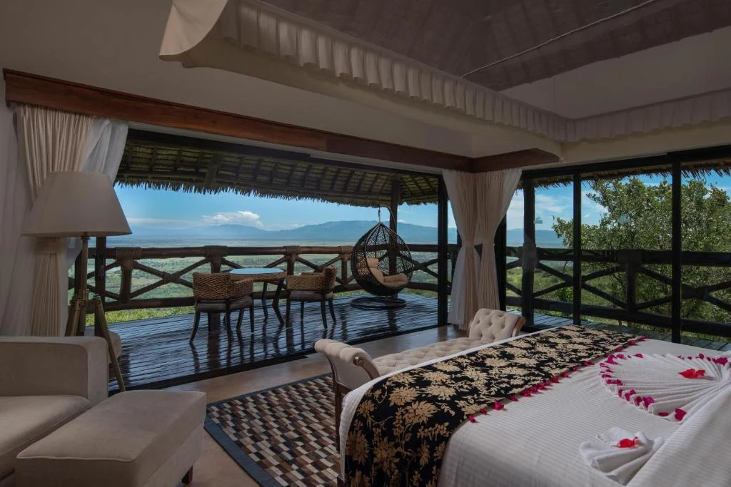 a bedroom with a bed and a balcony with a view at Wellworth Lake Manyara Kilimamoja Lodge in Mto wa Mbu
