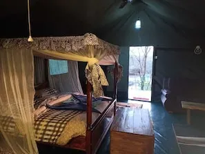 A tent-style room with a four-poster bed, a wooden bench, and a view of the outdoors. - Mara Duma Bush Camp (Maasai Mara)