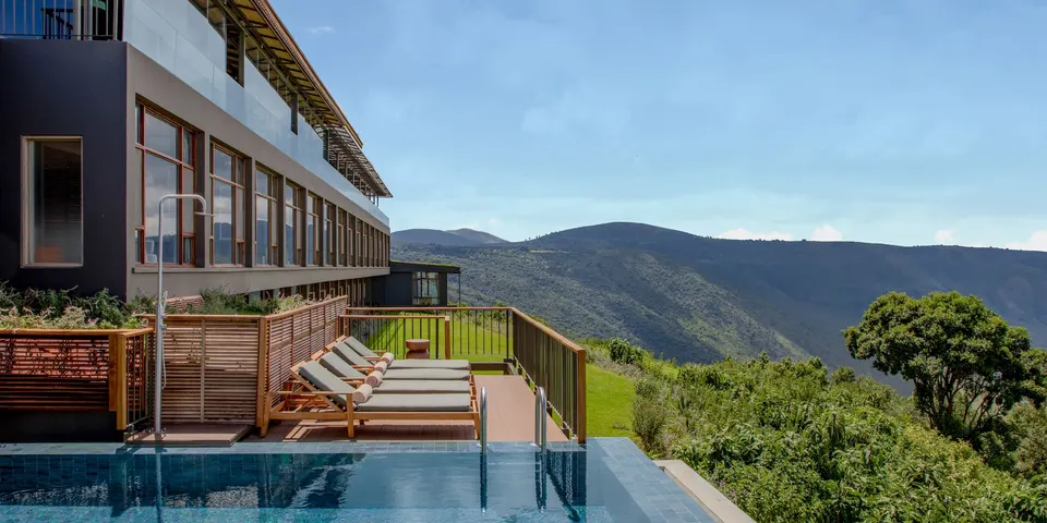 Modern hotel with infinity pool overlooking mountain view and sun loungers.