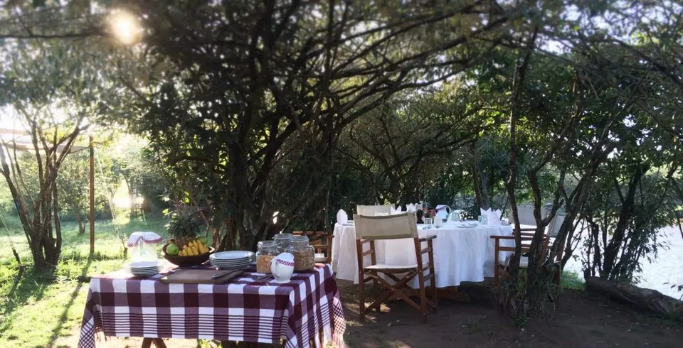Nkorombo breakfast tables beneath riverside trees